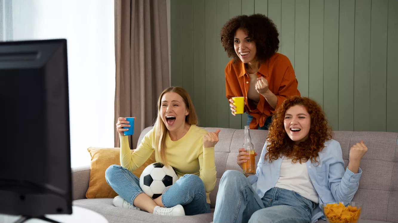 três mulheres assistindo futebol sentadas