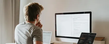 Jovem, de costas, trabalha usando computador, laptop e tablet conectados à sua internet residencial