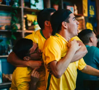 Homens vestidos com a camisa do Brasil comemoram gol enquanto assistem a futebol a vivo