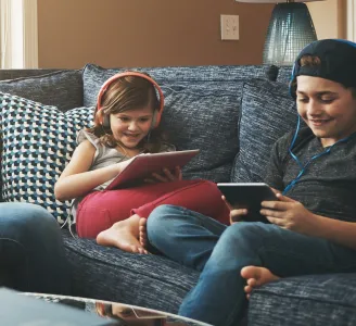 Duas crianças sorridentes sentadas no sofá usando tablets com Oi Fibra 500 Mega