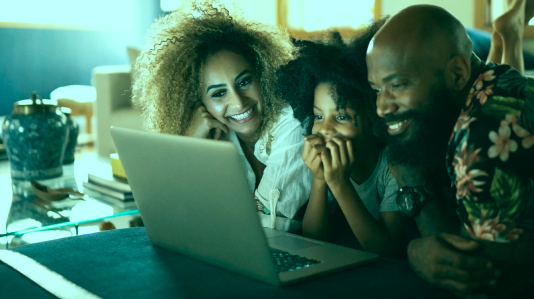 Família sorridente assistindo a algo divertido no notebook com expressões de alegria usando a internet de alta velocidade da Oi Fibra.